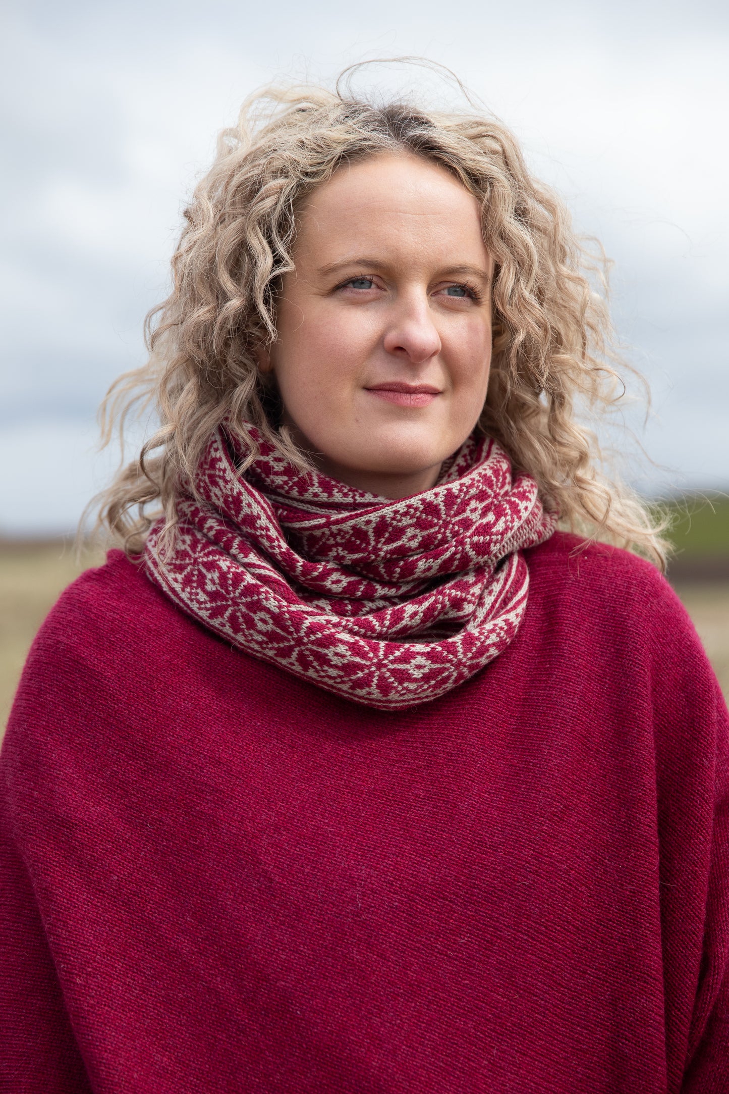 
                  
                    Woman wearing all over fair isle snood in Hibiscus and Mushroom colourway on an Orkney beach.
                  
                