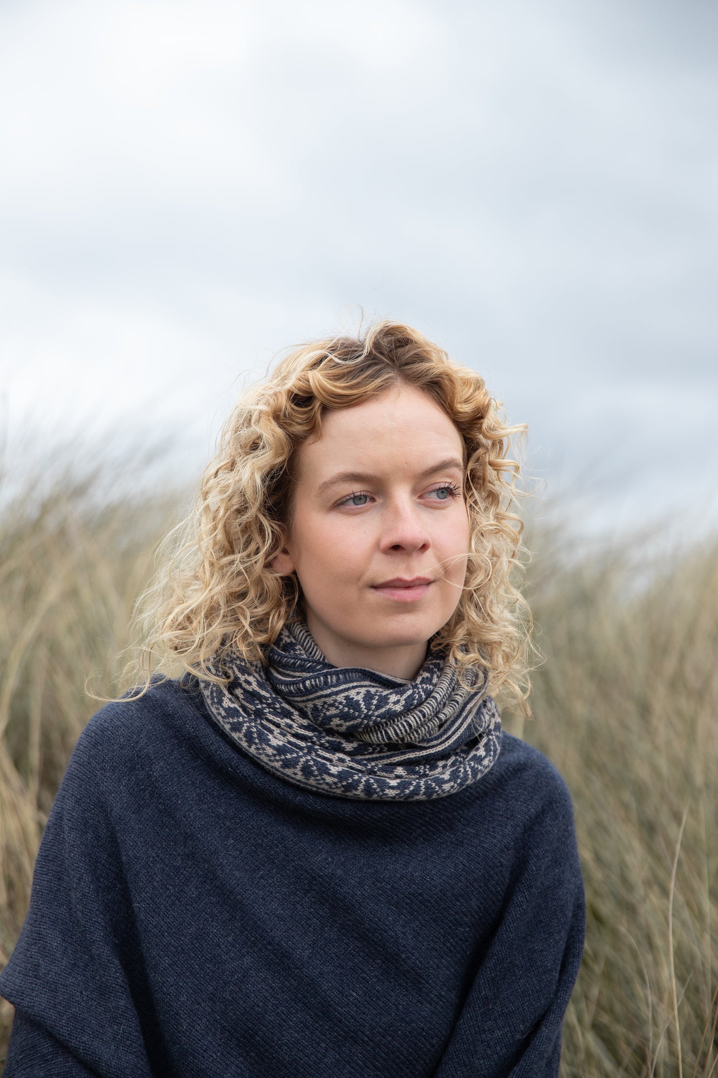 
                  
                    Woman wearing all over fair isle snood in Navy and Mushroom colour way on an Orkney beach
                  
                