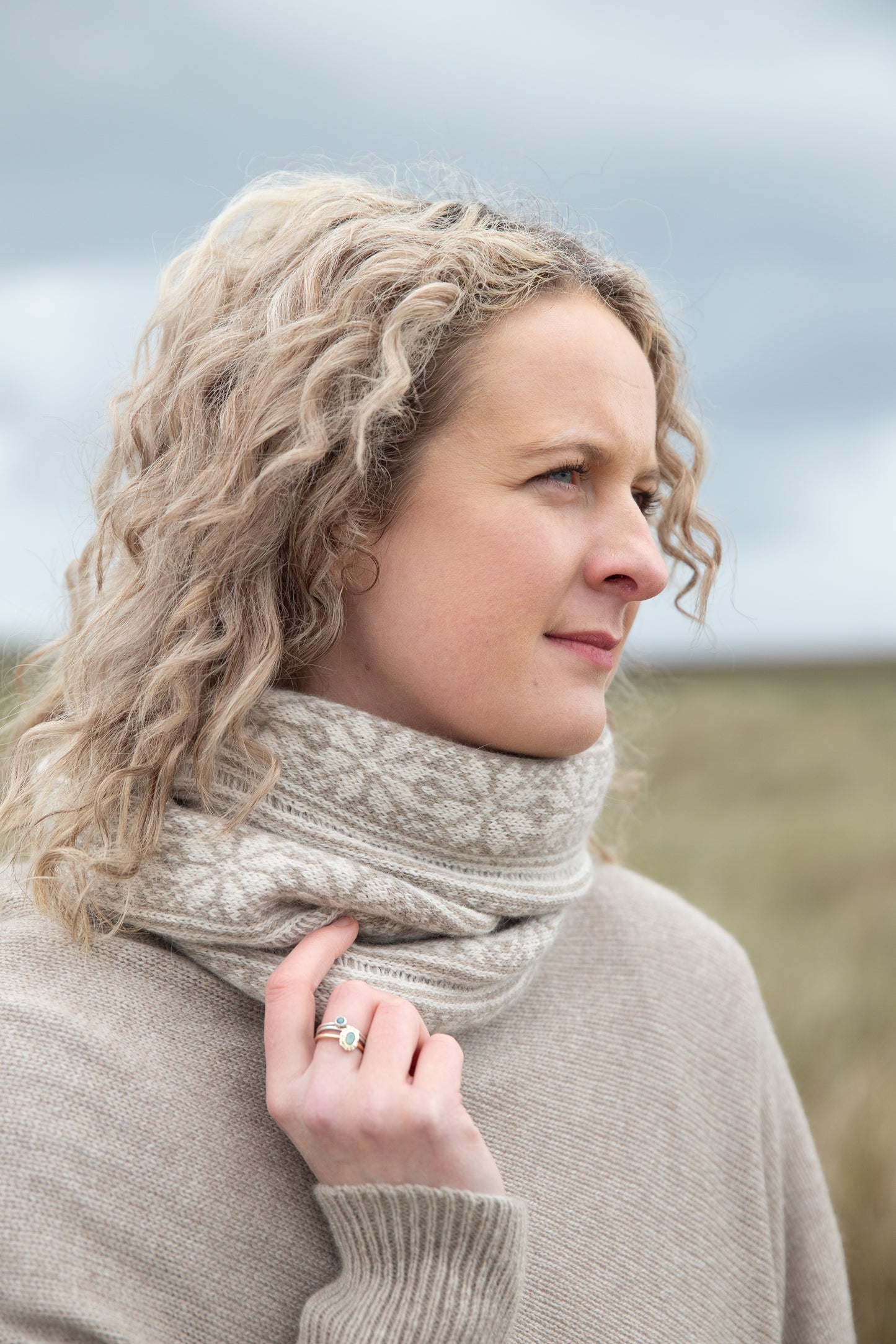 
                  
                    Woman wearing all over fair isle snood in mushroom and natural colour way on an Orkney beach
                  
                